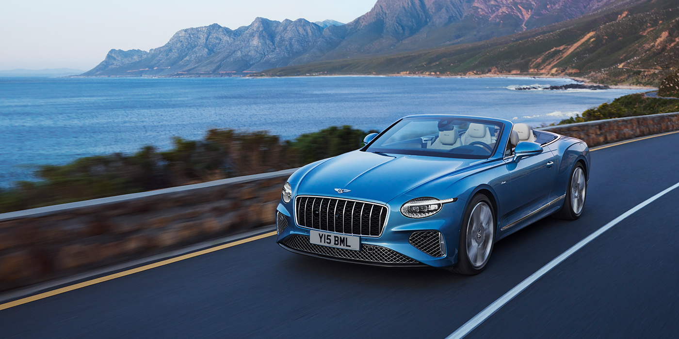 Bentley Lugano New Bentley Continental GTC Azure convertible in Light Windsor blue paint with 22 inch Azure wheels and chrome grill, driving dynamically by the sea