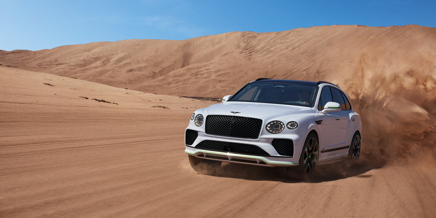 Bentley Lugano Bentley Bentayga Speed SUV front three quarter in Snow Quarts Pearlescent by Mulliner white paint driving dynamically through the desert
