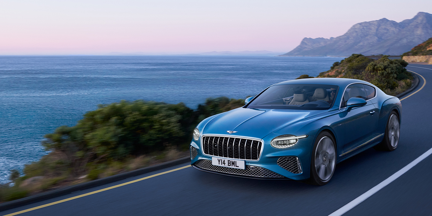 Bentley Lugano New Bentley Continental GT Azure coupe in Light Windsor blue paint with 22 inch Azure wheels and chrome grill, driving dynamically by the sea