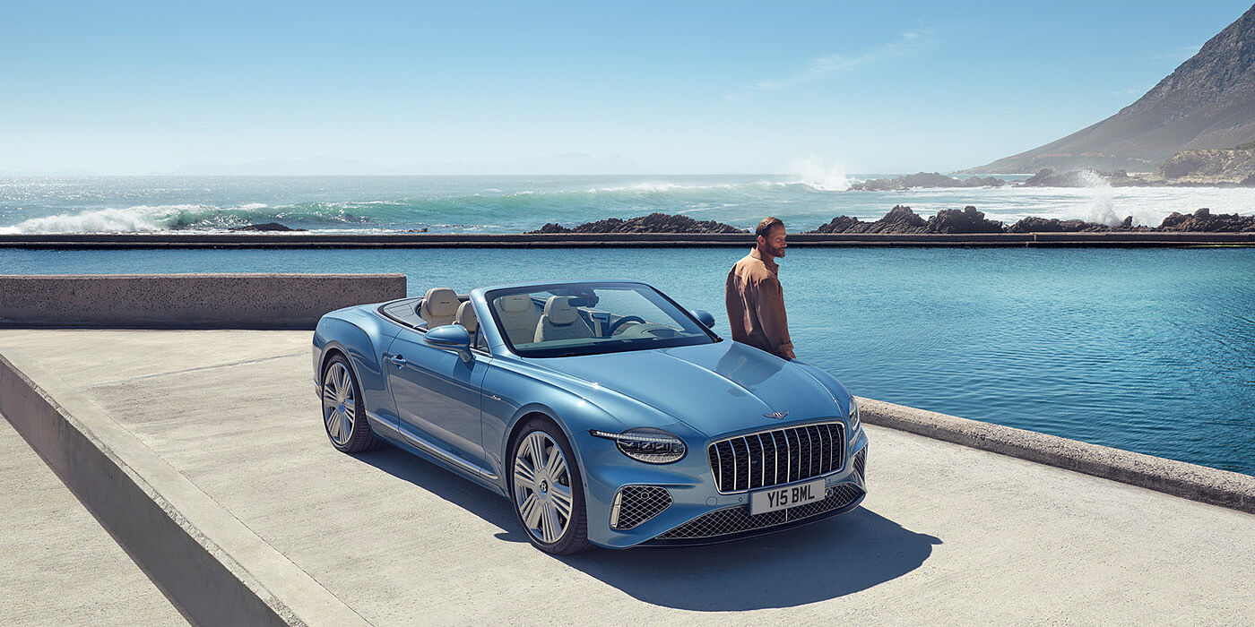 Bentley Lugano New Bentley Continental GTC Azure convertible front view in Light Windsor blue paint with 22 inch ten spoke wheels parked by the sea in the sunshine