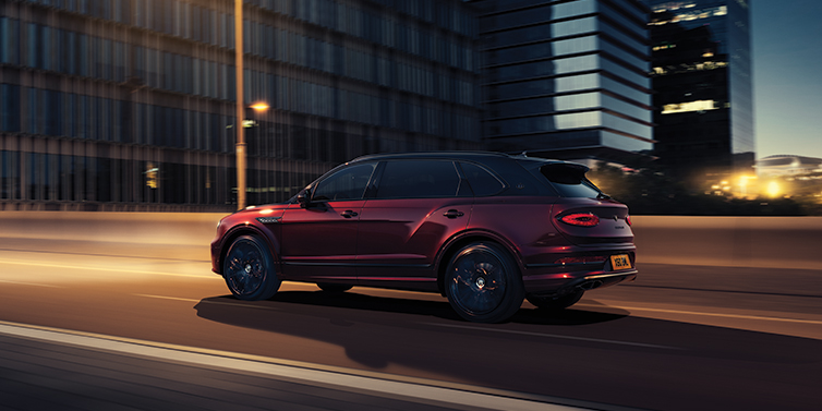 Bentley Lugano Bentley Bentayga Extended Wheelbase Mulliner SUV in Cricket Ball red paint driving dynamically in city at night
